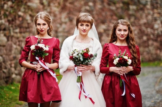 Two bridesmaids dressed for a Christmas wedding in red dresses either side of a bride