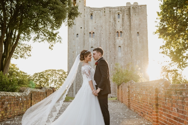 Bride and groom hold hands in front of Hedingham Castle as the sun sets