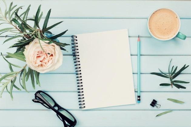 Blank notepad on a stylish wooden table with glasses, flower, pencil and a coffee