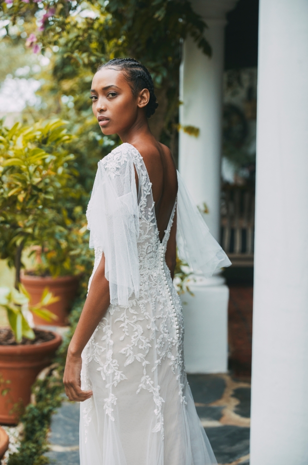 Model wears gown with v-back neckline and billowing sleeves