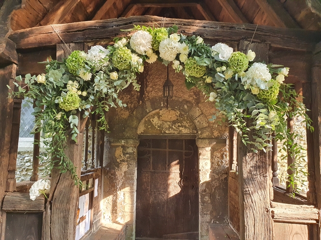 White and green wedding flowers decorating a rustic arch by Alison White Wedding Flowers