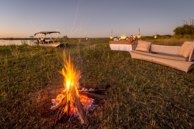 sofa on the grass next to a table and a lit campfire early evening 