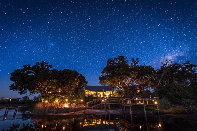 camp lodge at night by the creek lit up by lamps as it's dark