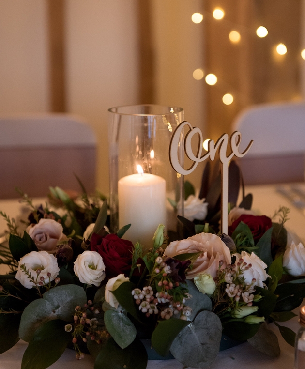 Winter wedding table centrepiece with flowers, candle and gold table number