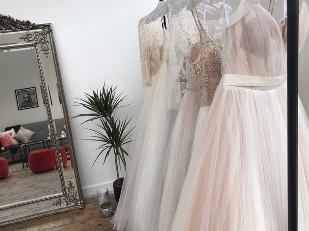 Wedding dresses on a rail in front of ornate mirror.