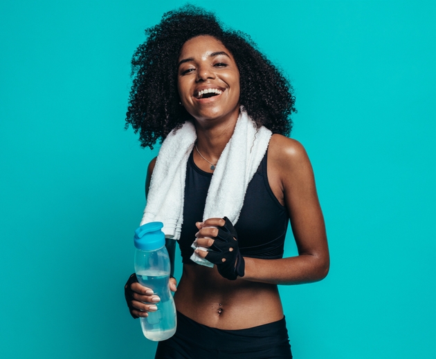 Girl after workout with towel and water bottle on turquoise background.