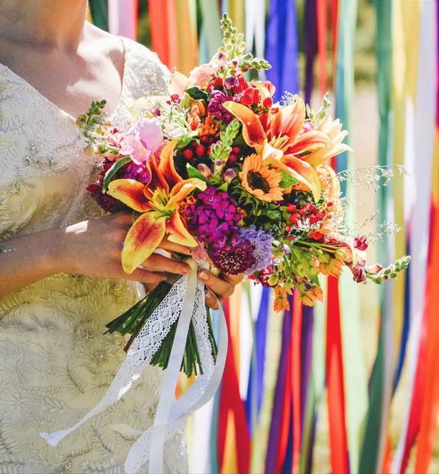 Bride with colourful bouquet in front of rainbow ribbon backdrop