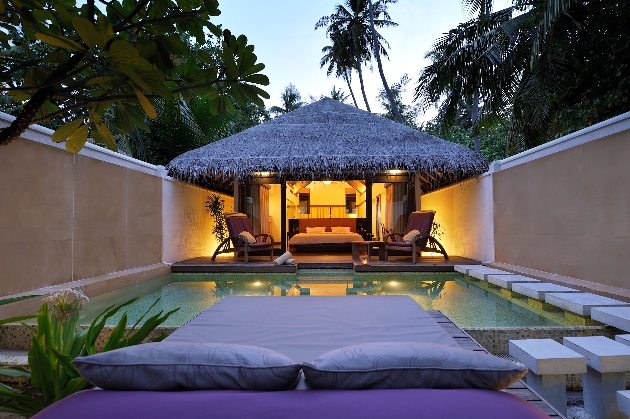lounge bed by pool at night with view of hut lit up 