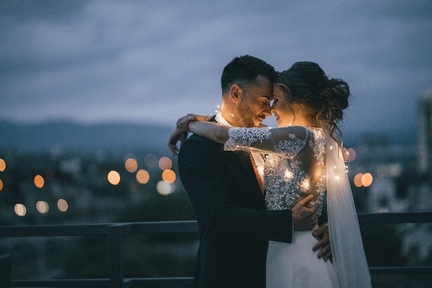 bride and groom embracing on a terrace wrapped in fairlights