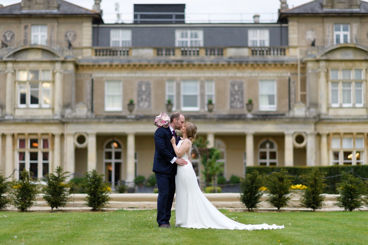 wedding couple standing on the grass in front of a mansion house 