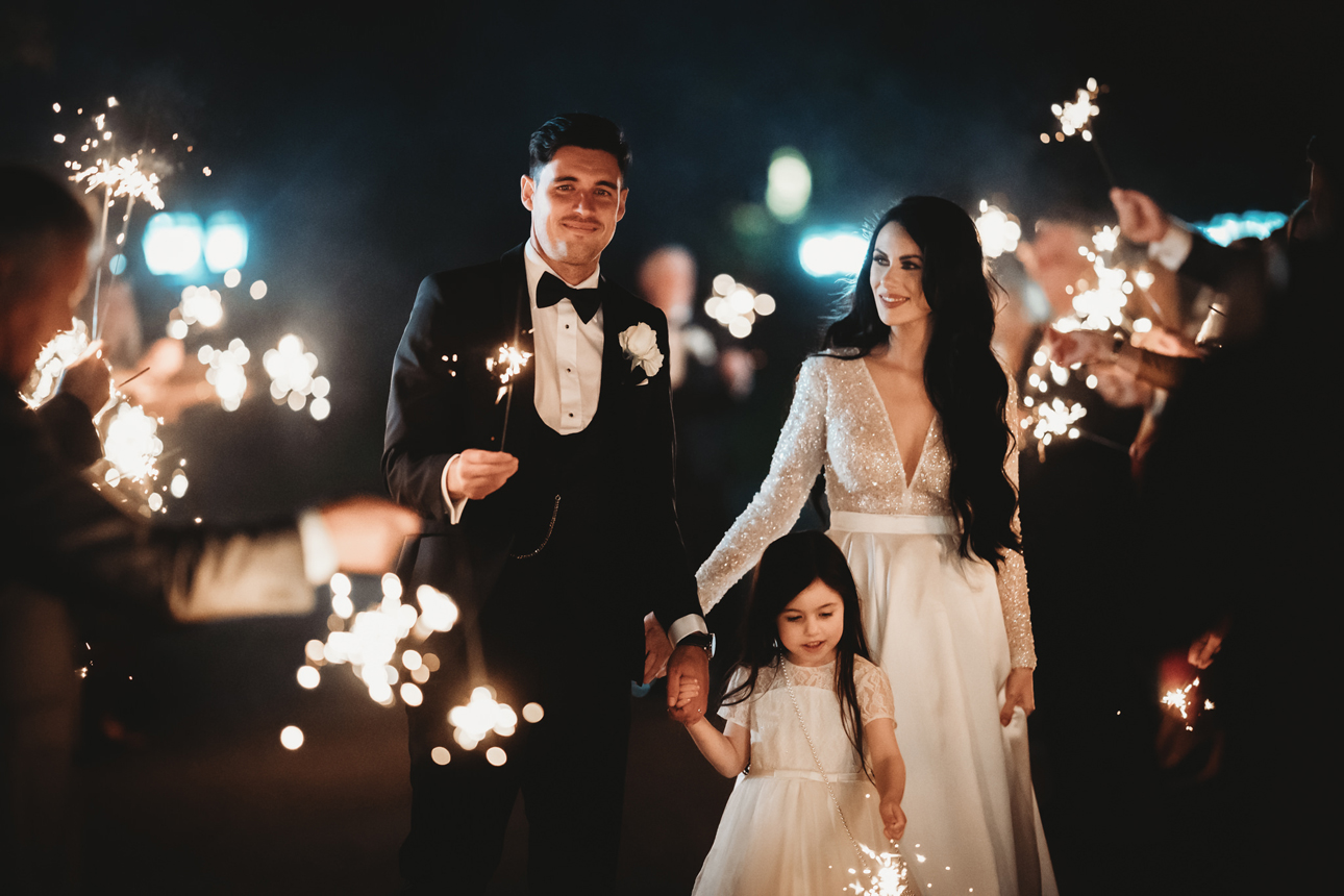 Bride, groom and daughter surrounded by friends holding sparklers