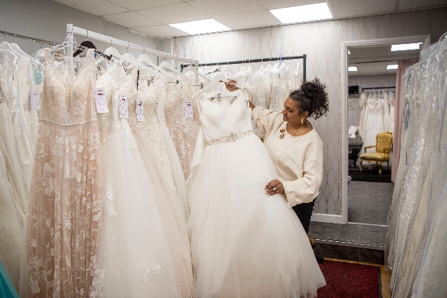 woman in a wedding dress shopping hold up a dress off the rack