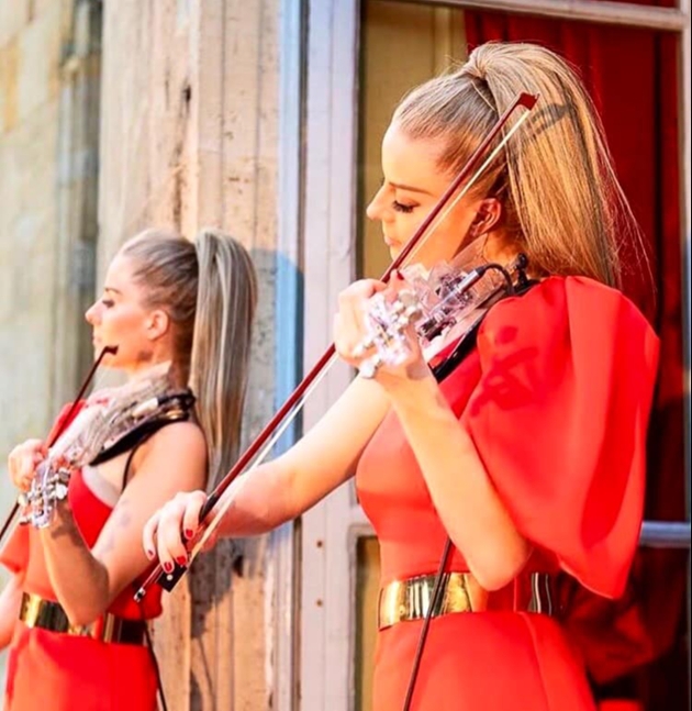 two women wearing identical red dresses playing violins