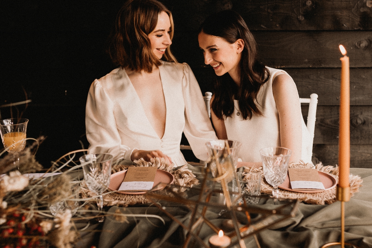 two women in wedding dresses sat at a table decorated with wedding setting items