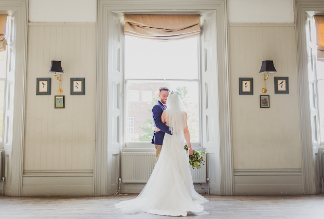 bride and groom standing in front of a window in a stately room