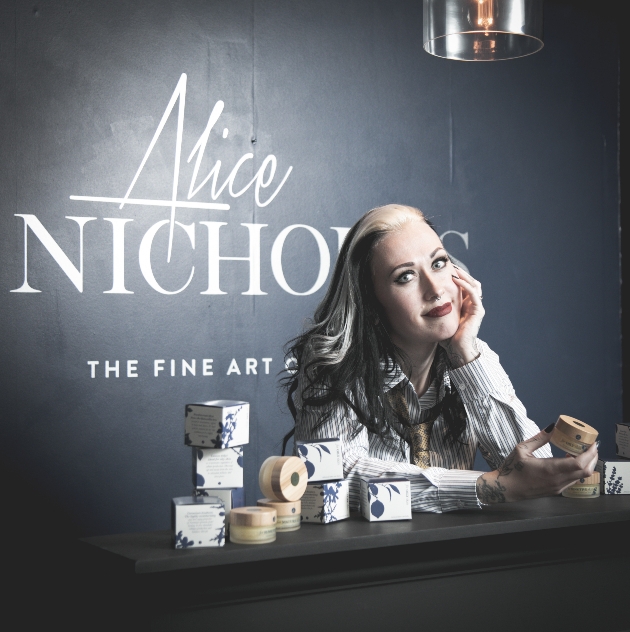 Alice Nicholls leaning on a counter holding a pot of balm in her hand