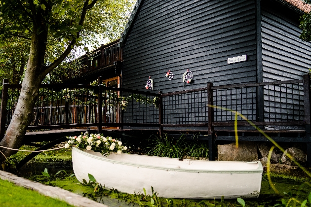 white wooden boat in stream outside black wooden a barn