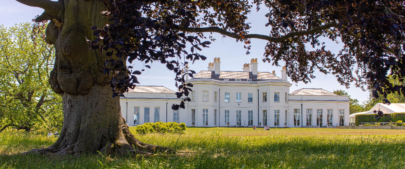 elegant white Neoclassical façade of manor house with grass and trees in view