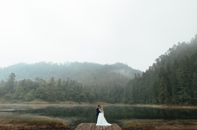 wedding couple on a jetty by a lake with mountains in the background