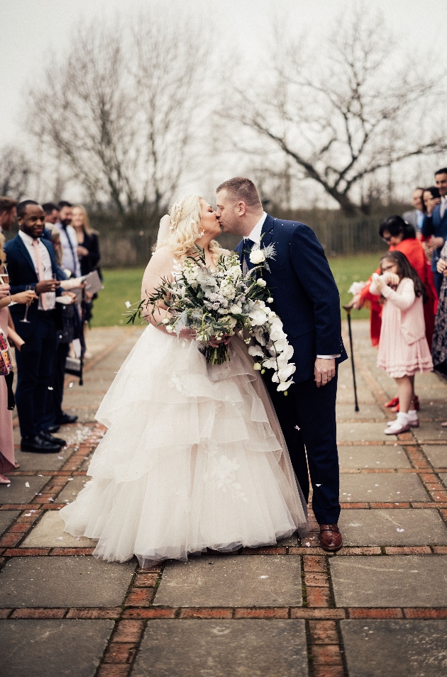 couple in wedding dress and navy suit on a grey winters day having their confetti shot moment