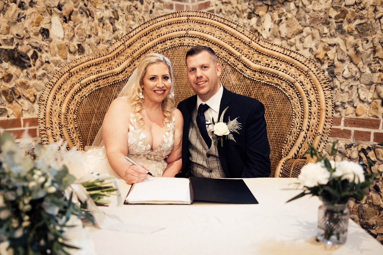 Essex wedding couple in their wedding attire sat in a wicker chair signing the register