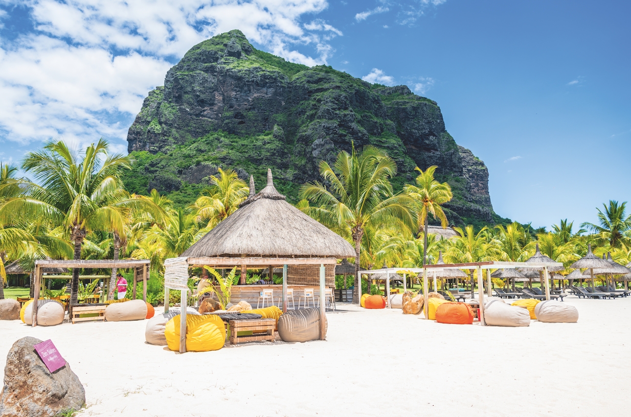 large rock behind beach with parasols and palm trees