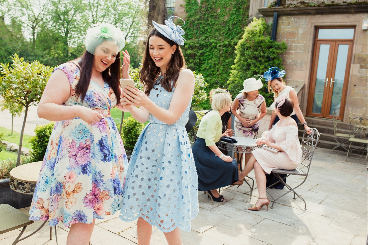 two wedding guests looking at a phone together standing outside