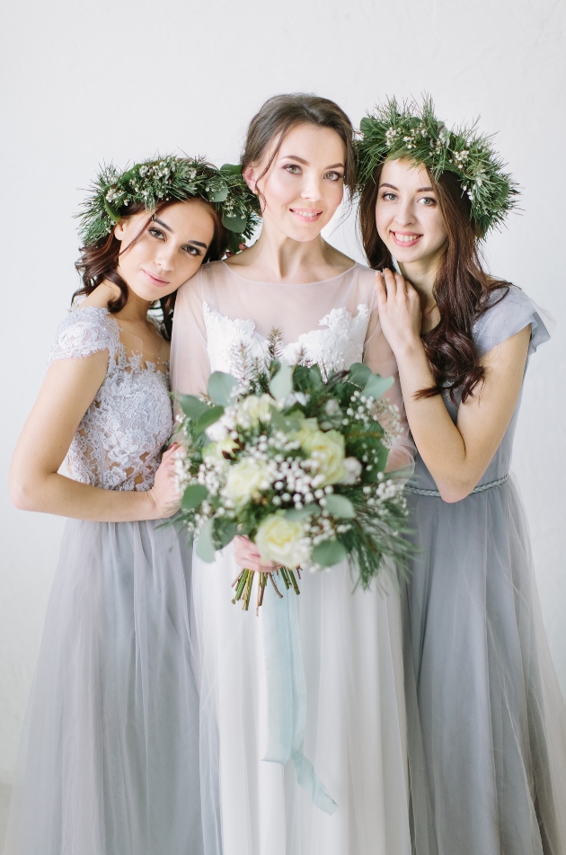 bride standing with two bridesmaids in grey dresses and floral head dresses