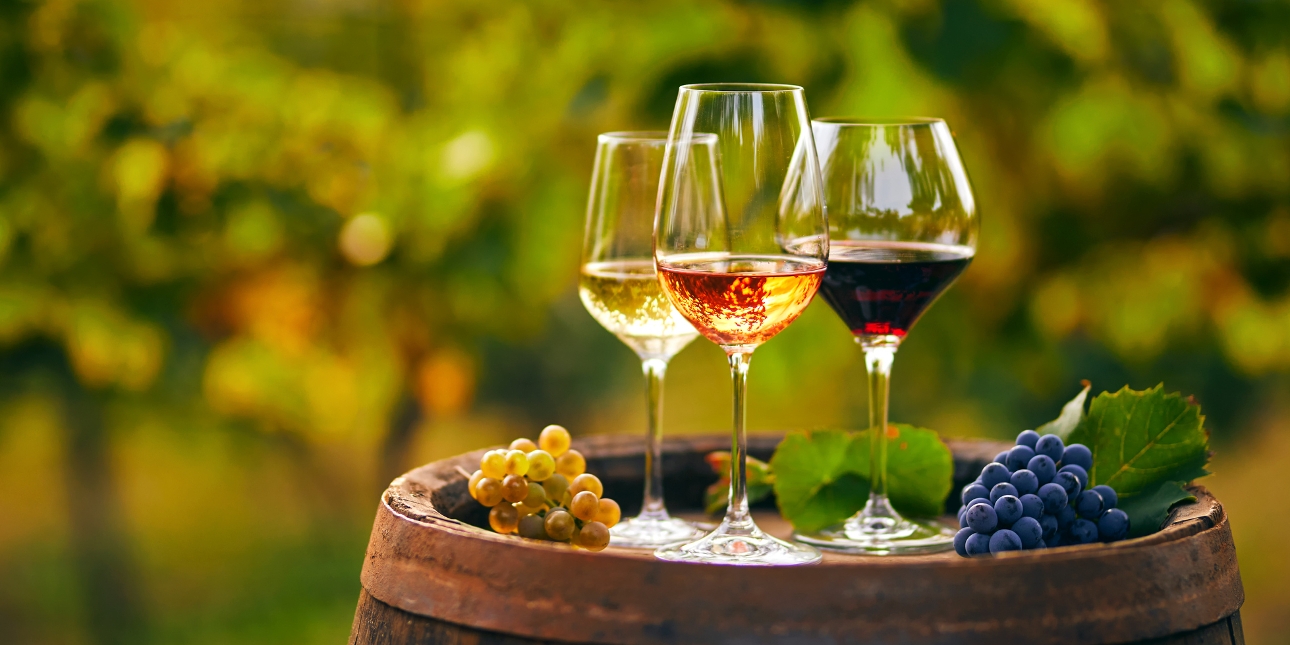 three wine glasses with red white and rose in on a barrel in a vineyard