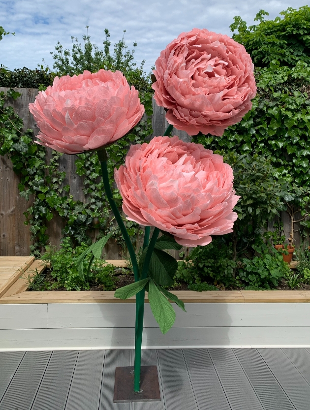 three large paper pink flowers on stems about 4ft high