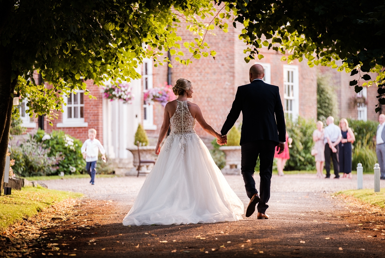 bride and groom walking towards their wedding venue under some trees