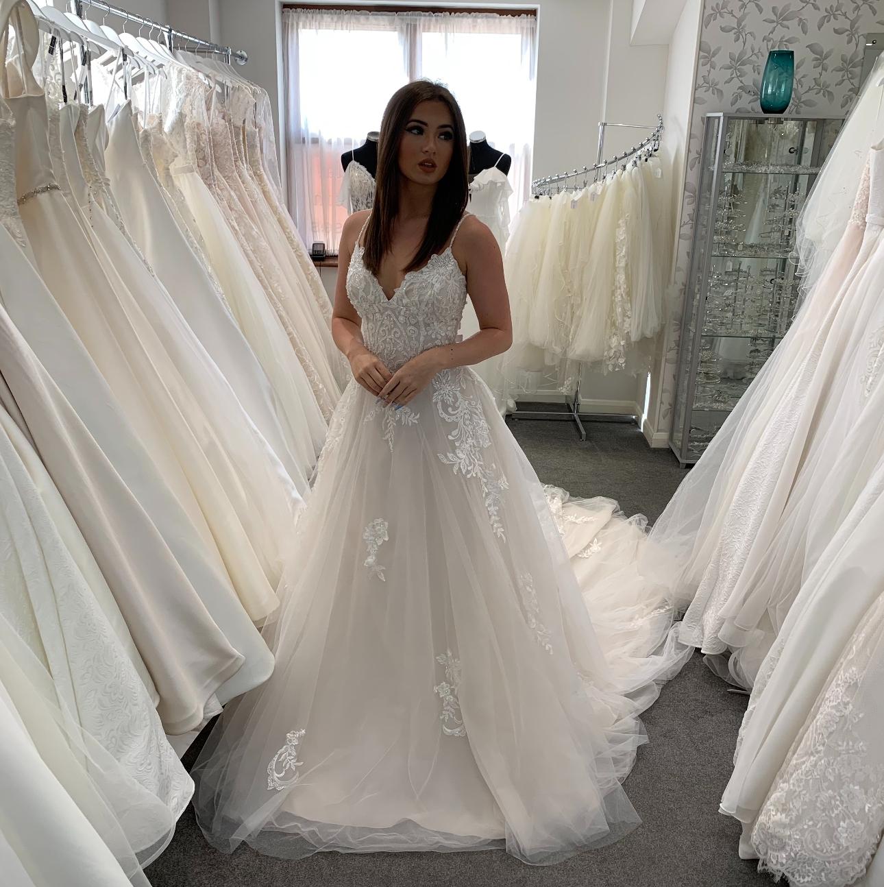 model in wedding dress in wedding shop surrounded by lots of dresses