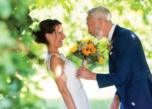 bride and groom standing together he is holding her bouquet of sunflowers