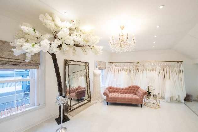 interior of boutique plush pink sofa large, gilded mirror dress rail of clothes