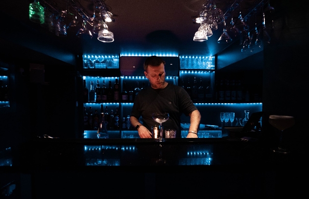 man standing behind a black bar with blue lights darkly lit room