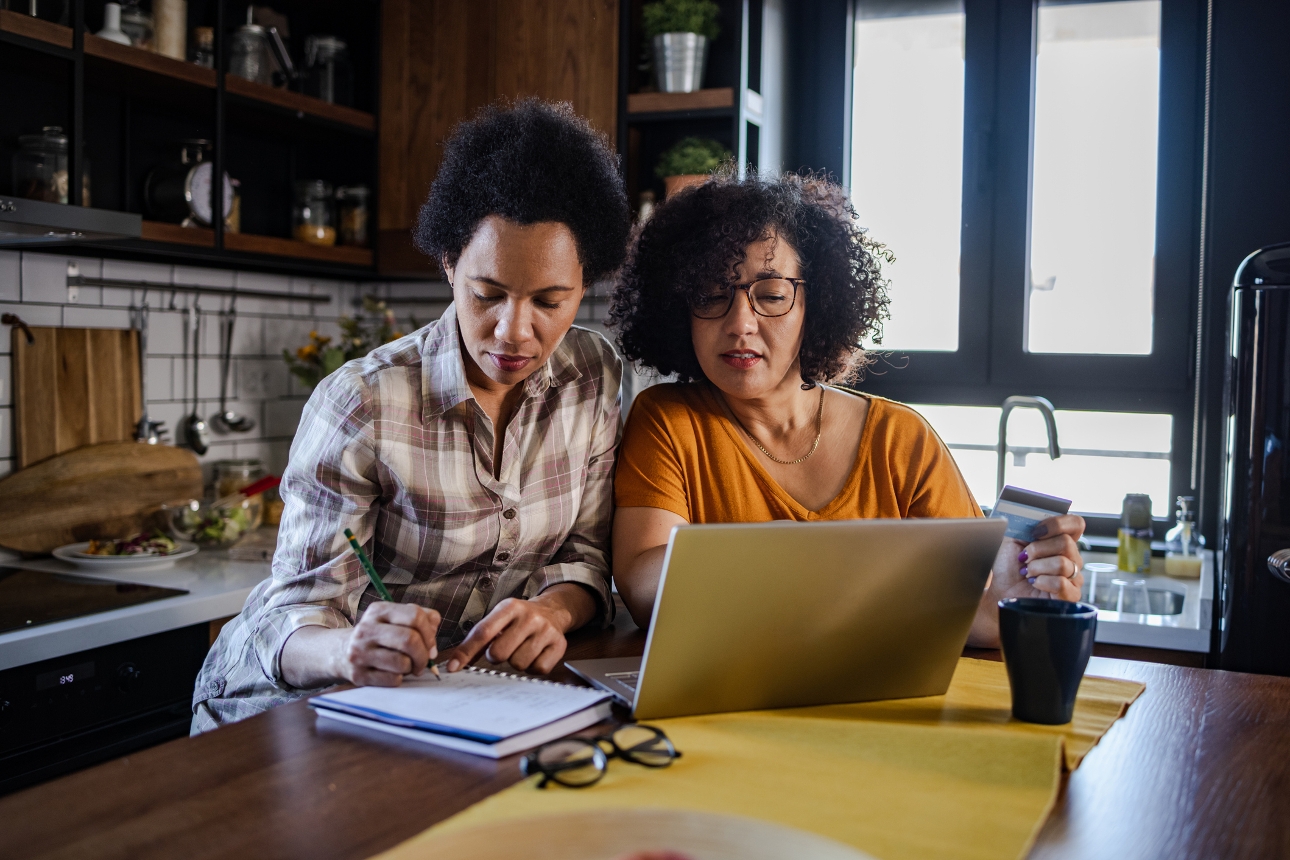 two women at a kitchen counter looking at laptop and planning things out