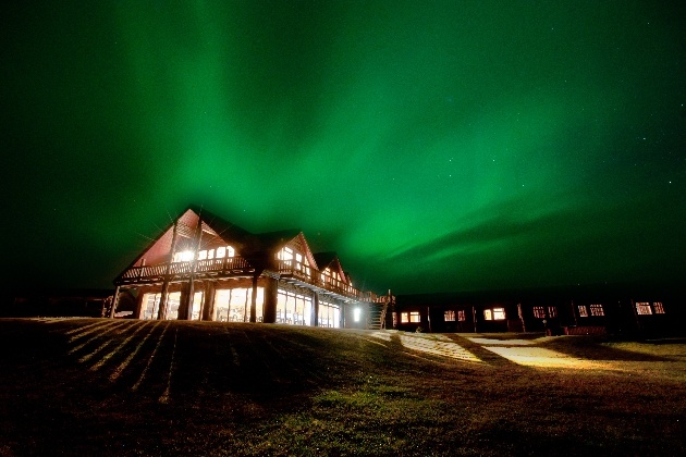 chalet hotel at night with northern lighst in the sky turning it green