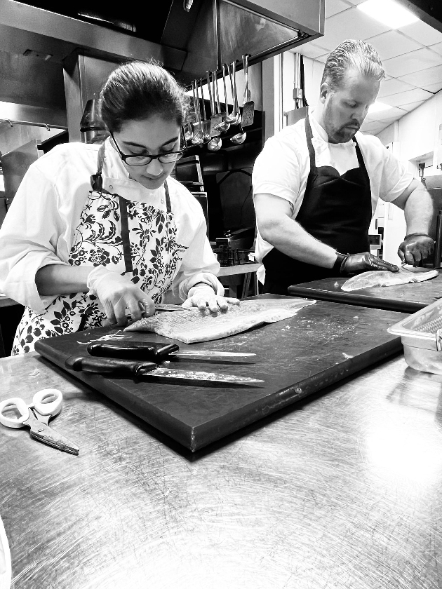 black and white image of chef in kitchen with student