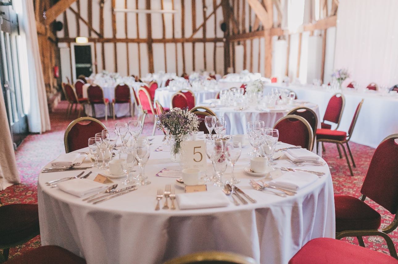 round tables set up at reception with white clothes, red chairs and red carpet