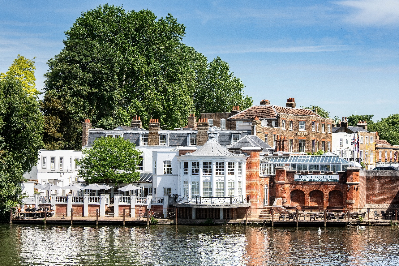 Riverside hotel, red brick and white facade, terrace, and table and chairs by river