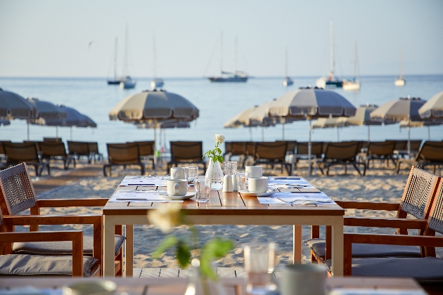 Four wooden chairs placed in front of a table on the beach