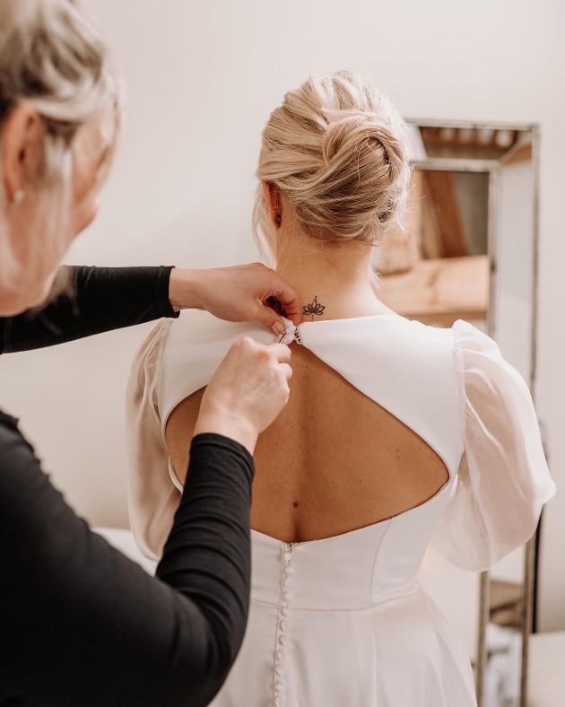 woman helping bride in dress doing buttons up at back