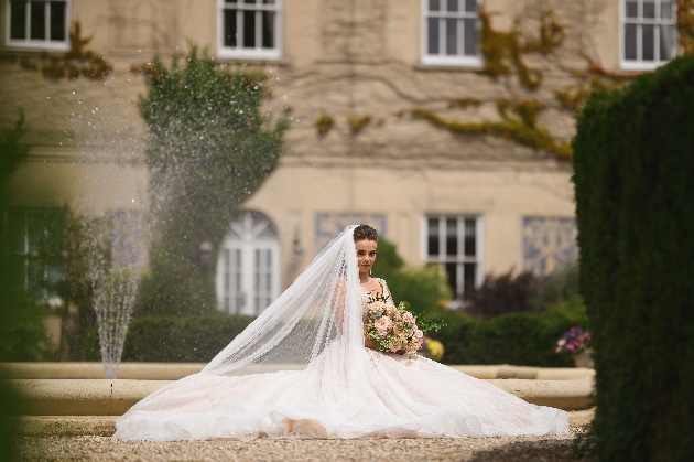 bride sitting down in huge bridal dress in front of fountain