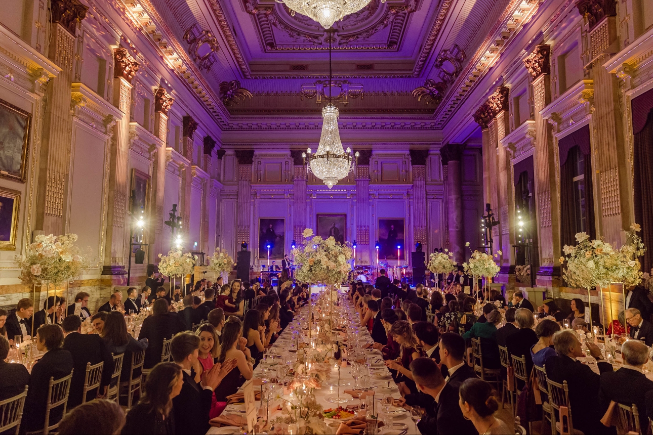 grand reception room with long tables and chandelier in centre large tall floral displays