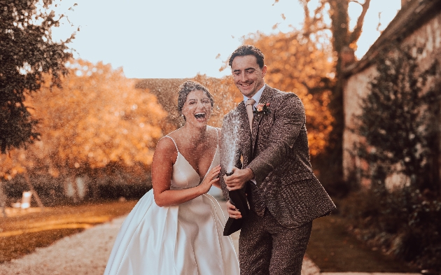 bride and groom popping bottle of champagne
