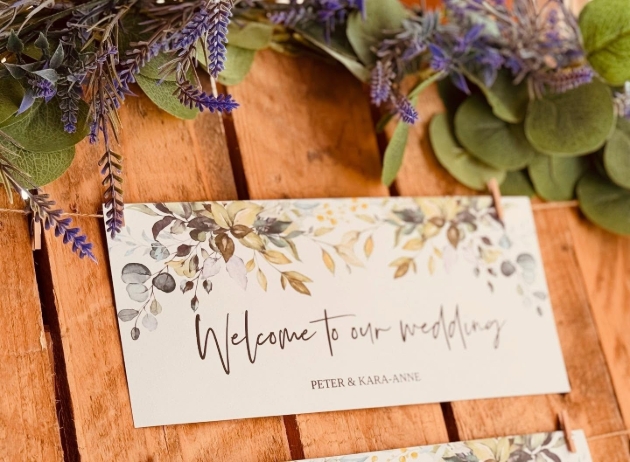 close up shot of rustic wooden wedding table plan with purple flowers