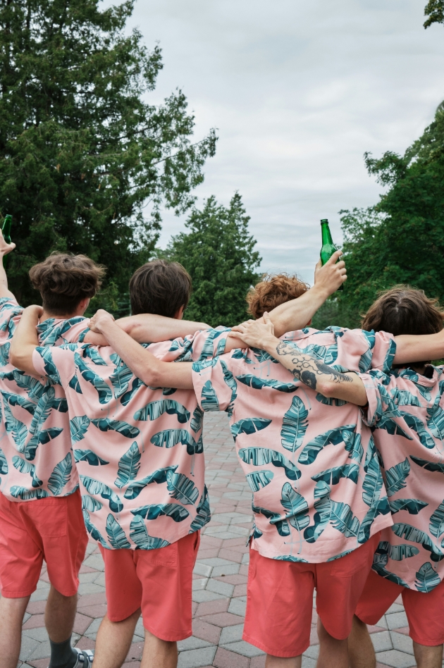 four men in matching outfits embracing with a beer outside