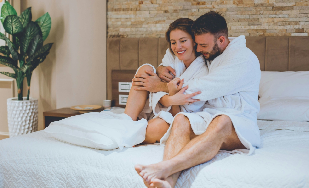 couple in bathrobes cuddling on a bed in hotel
